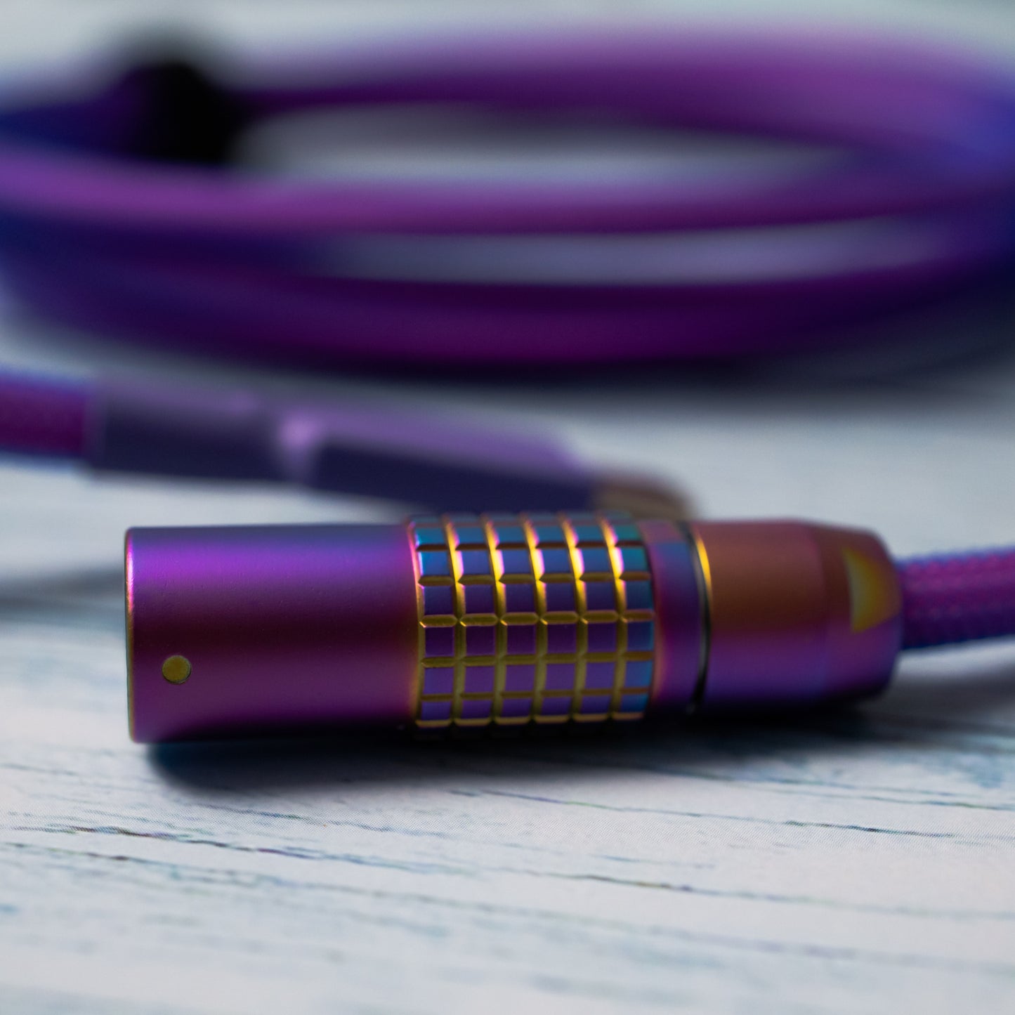 Closeup of rainbow FEMO 1B connector. In the background, out of focus, a bundled mechanical keyboard cable in Teleios purple sleeving, blue TechFlex, and a USB C connector with purple heat-shrink tubing.