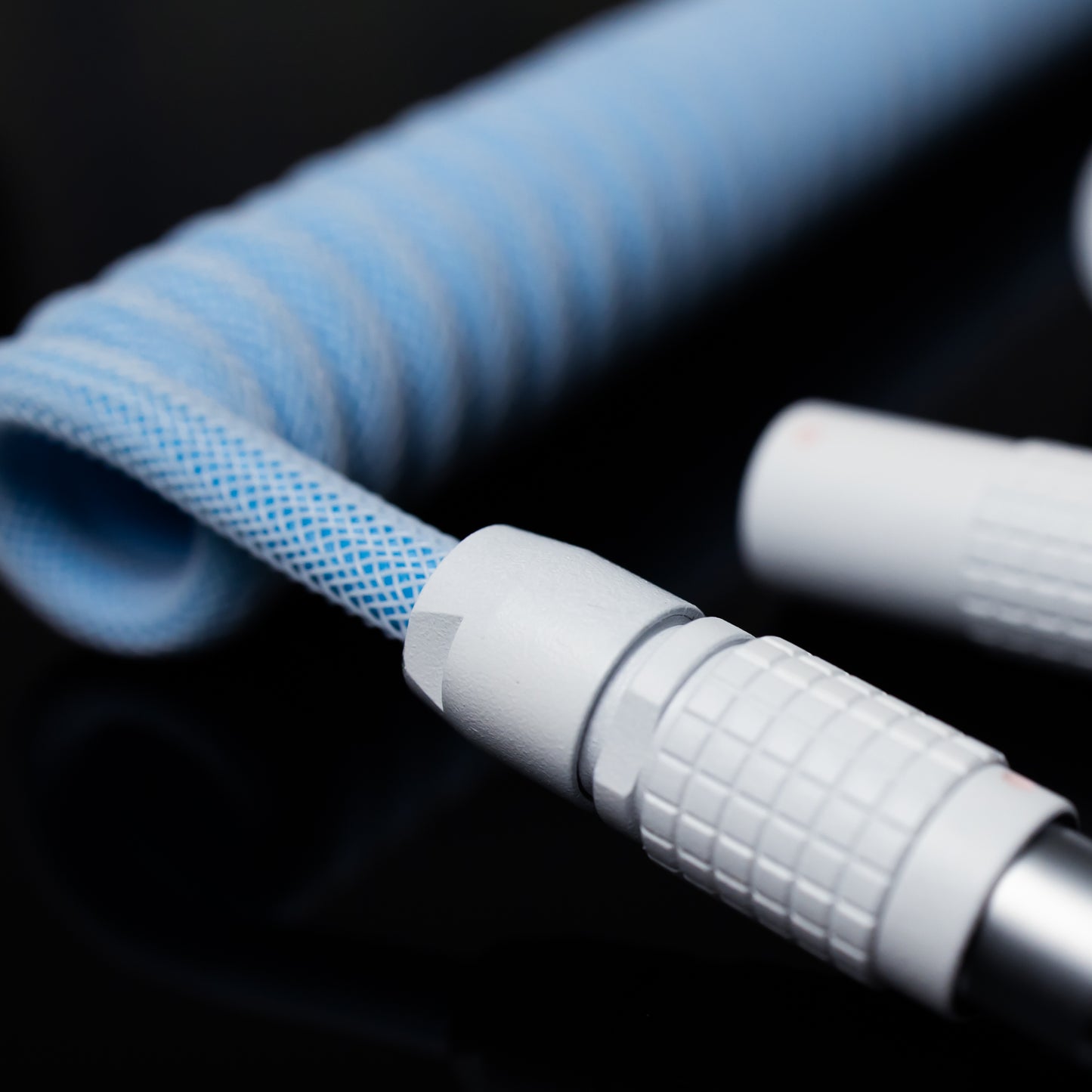 Closeup of FEMO 1B chuck in sandblasted white. In the background, coiled end of the cable in Teleios Aqua Blue, the straight end in Teleios Polar White, and white TechFlex.