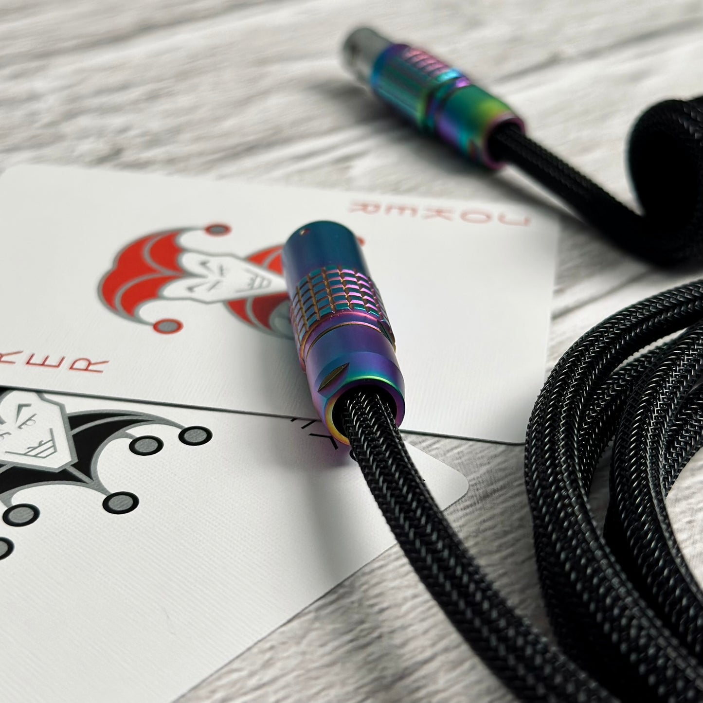Closeup of two joker cards (one red & one black), Teleios sleeved keyboard cable in black with black TechFlex, and a rainbow colored FEMO push/pull connector