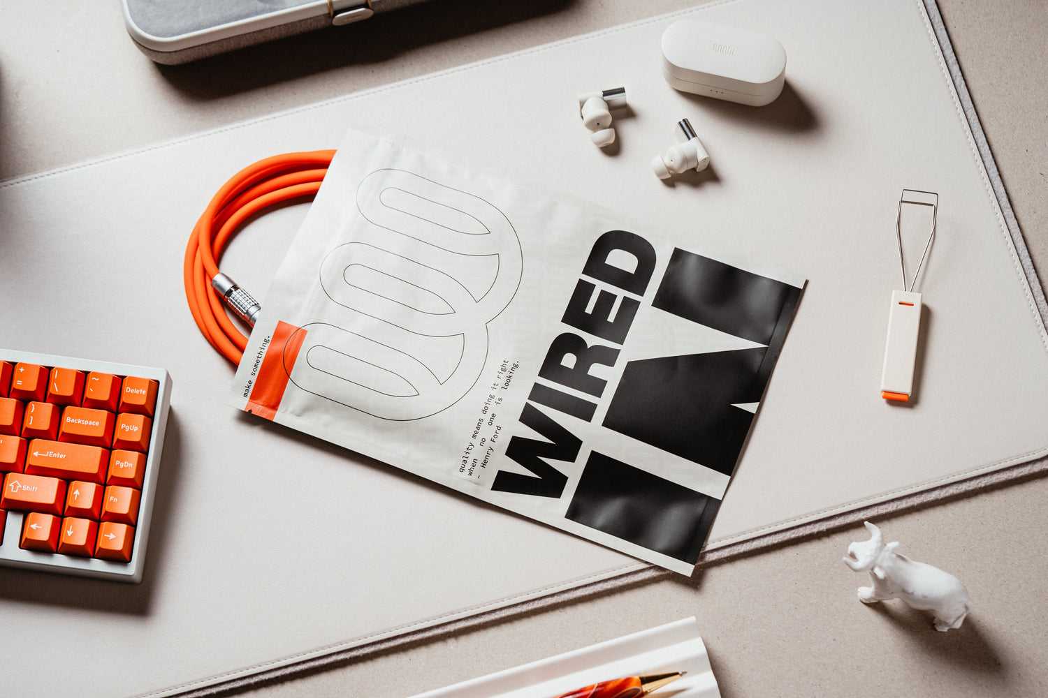 Picture of 8-core mechanical keyboard cable coming out of a high quality Wired In heat seal bag next to a mechanical keyboard with GMK Dolche, a notebook with a red pen, a black and red switch opener, and a wool snow hat