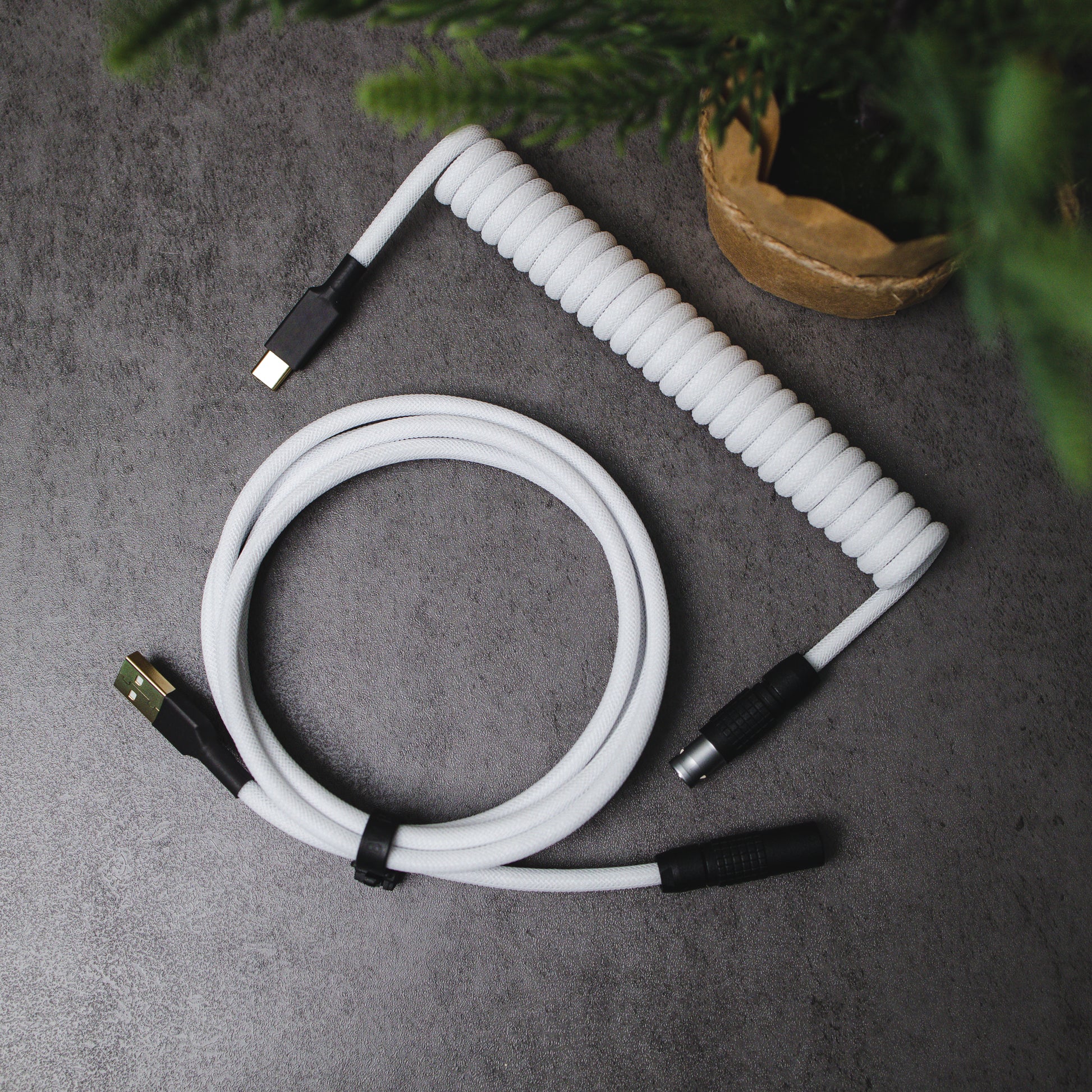 Birds eye view of white and black coiled mechanical keyboard cable. Teleios Polar White sleeving, white TechFlex, black heat-shrink tubing, gold USB A and USB C connectors, black sandblasted FEMO 1B push/pull connector.