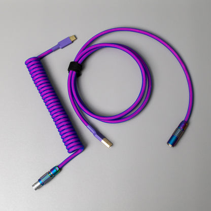 Birds eye view of coiled mechanical keyboard cable with FEMO push/pull connector in Rainbow, Teleios pink sleeving, blue TechFlex second layer, and purple heat-shrink tubing over gold USB A and USB C connectors