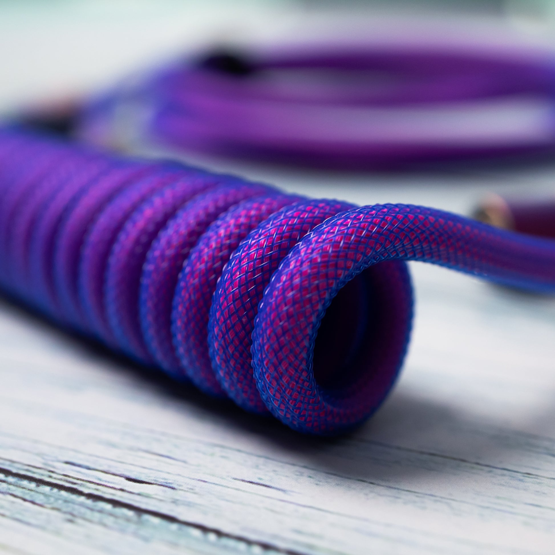 Closeup of the coil part of a coiled mechanical keyboard cable with FEMO push/pull connector in Rainbow, Teleios pink sleeving, blue TechFlex second layer, and purple heat-shrink tubing over gold USB A and USB C connectors
