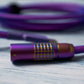 Closeup of rainbow FEMO 1B connector. In the background, out of focus, a bundled mechanical keyboard cable in Teleios purple sleeving, blue TechFlex, and a USB C connector with purple heat-shrink tubing. 