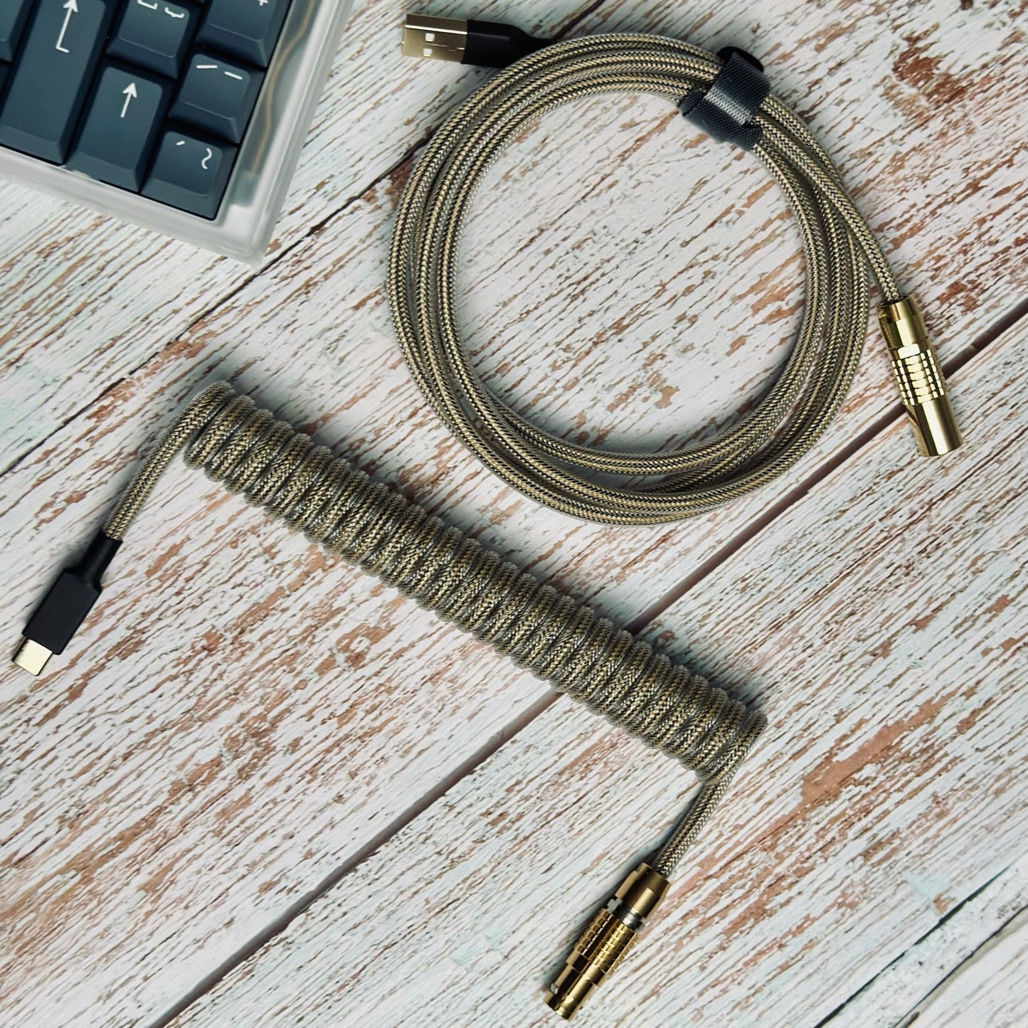 Birds eye view of coiled mechanical keyboard cable. Teleios Fusion black and gold sleeving, gold FEMO 1B push/pull connector, clear TechFlex second layer, gold USB A and USB C connectors with black heat-shrink tubing, and bundled with a black Velcro tie. 