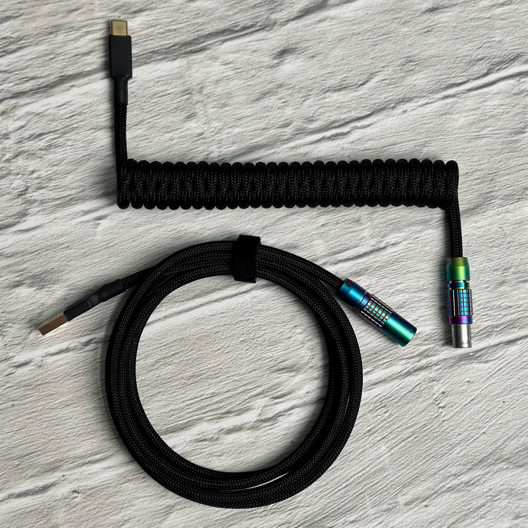 Birdseye view of coiled mechanical keyboard cable with black Teleios sleeving, black TechFlex second layer, and rainbow FEMO connector