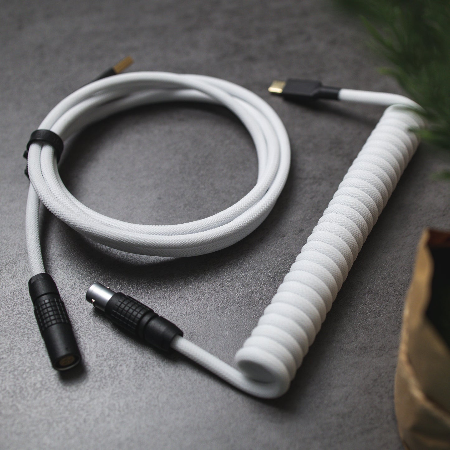 Side view of white and black coiled mechanical keyboard cable. Teleios Polar White sleeving, white TechFlex, black heat-shrink tubing, gold USB A and USB C connectors, black sandblasted FEMO 1B push/pull connector.
