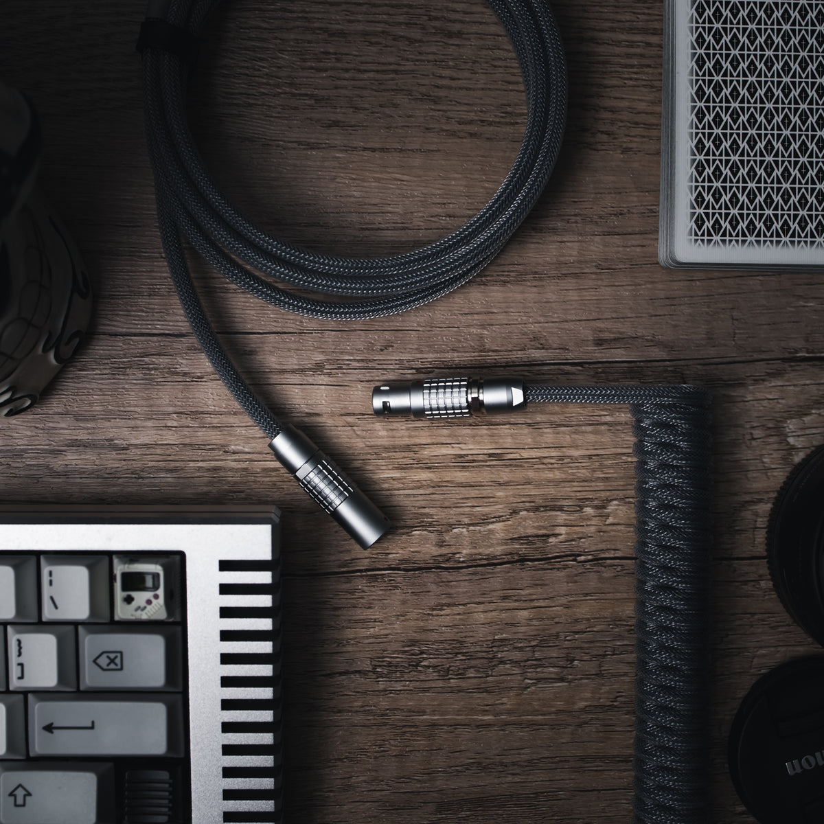 Birds eye view of custom mechanical keyboard coiled cable along with a deck of cards and RAMA Thermal keyboard. Teleios carbon grey/gray, TechFlex Clear, FEMO 1B push/pull connector, and bundled cable of the same type.